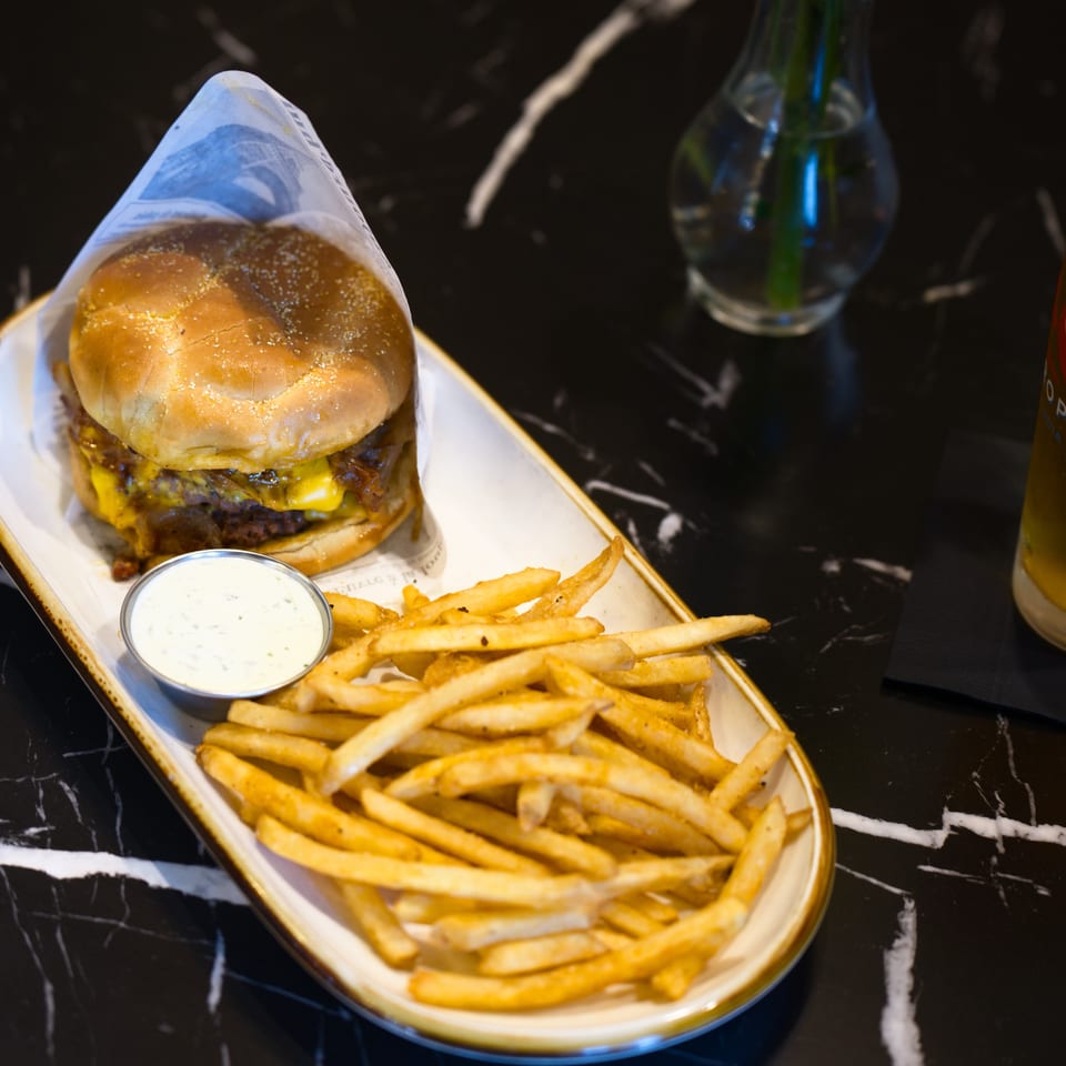 Cheeseburger with fries and dipping sauce served on a platter beside a glass of pale ale.