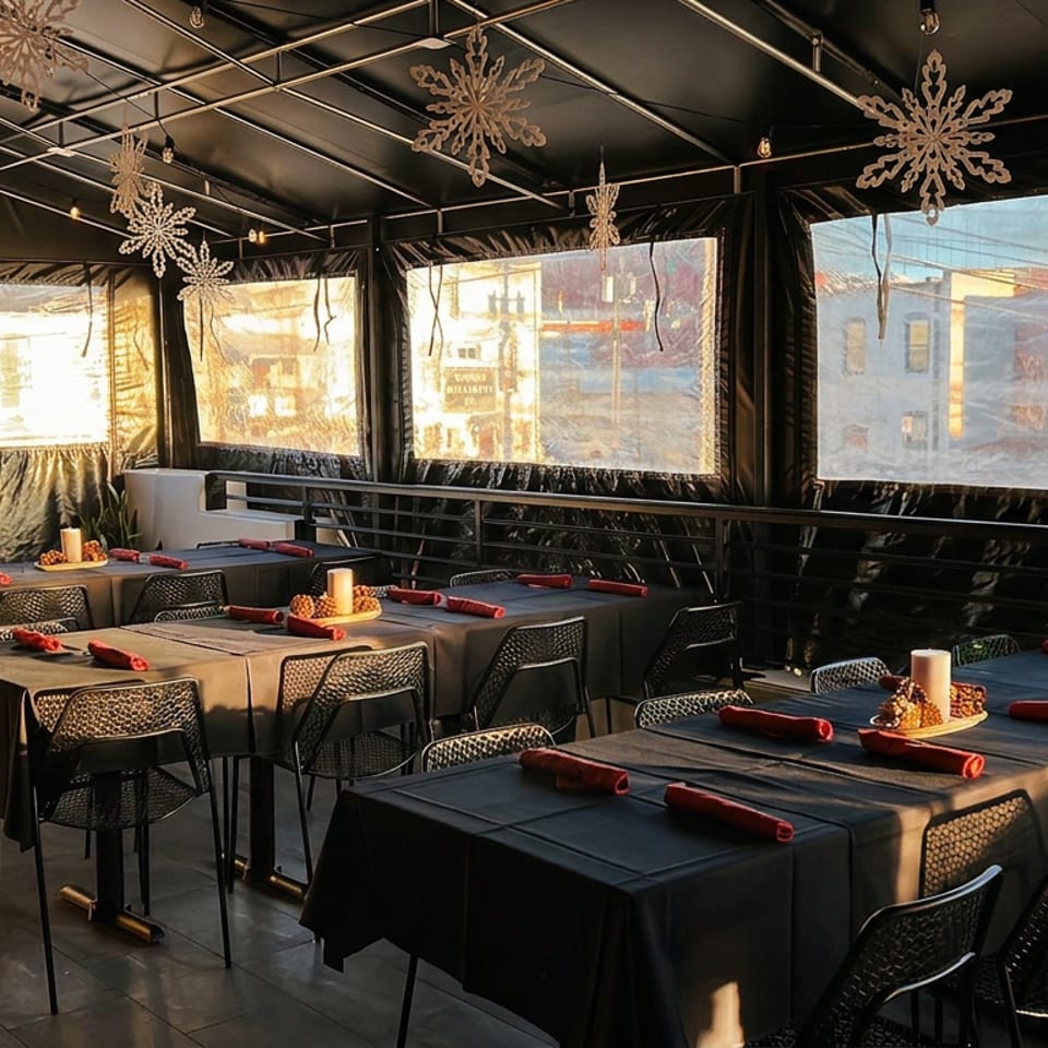Sunlit restaurant dining room with black tablecloths, red napkins, place settings, and hanging snowflake decorations.
